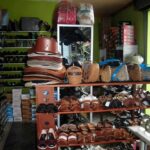Indoor shop with shelves of leather handbags, sandals, and sneakers arranged on wooden racks.
