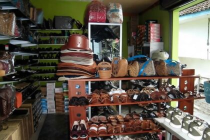 Indoor shop with shelves of leather handbags, sandals, and sneakers arranged on wooden racks.