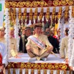 Group of men in traditional cream outfits with red sashes on a gold-decorated ceremonial float at a festival parade.