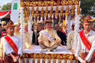 Group of men in traditional cream outfits with red sashes on a gold-decorated ceremonial float at a festival parade.