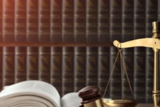 Gavel and gold scales of justice on a wooden desk with an open law book nearby.