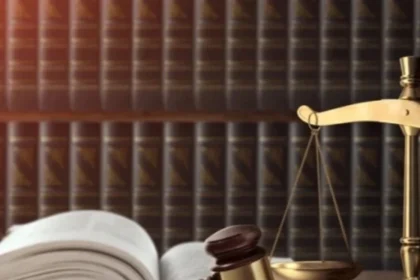 Gavel and gold scales of justice on a wooden desk with an open law book nearby.