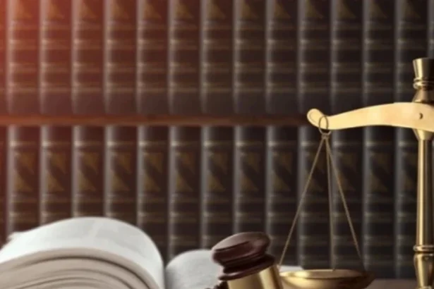 Gavel and gold scales of justice on a wooden desk with an open law book nearby.