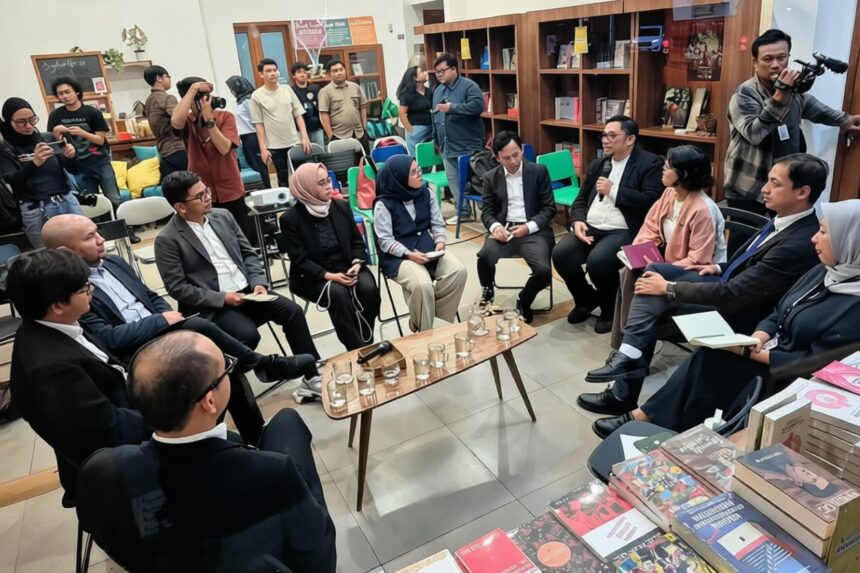 Group of professionals seated in a circle inside a bookstore, discussing with notebooks and phones while photographers document the event.