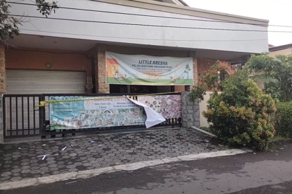 Front of a daycare center with banners across the gate, advertising Little Aresha and a daycare program Plus. A yellow caution tape runs along the fence.