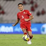 Soccer player in red jersey #5 dribbles the ball on a green field during a match.