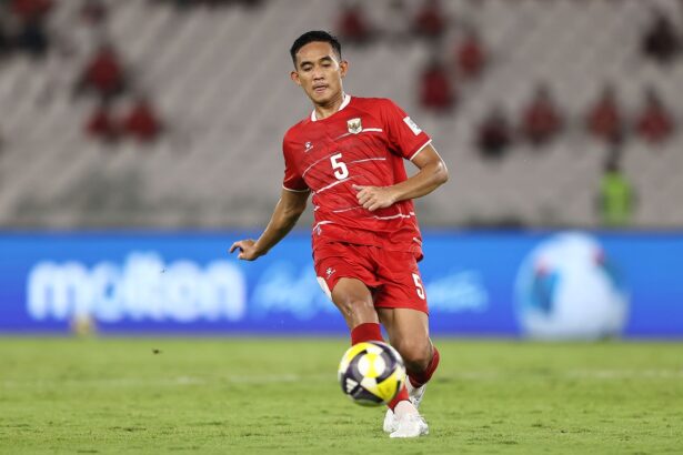 Soccer player in red jersey #5 dribbles the ball on a green field during a match.