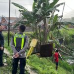 Police officers in bright vests stand by a canal as bystanders observe a rural scene with a child near the water and a tilted metal drum.
