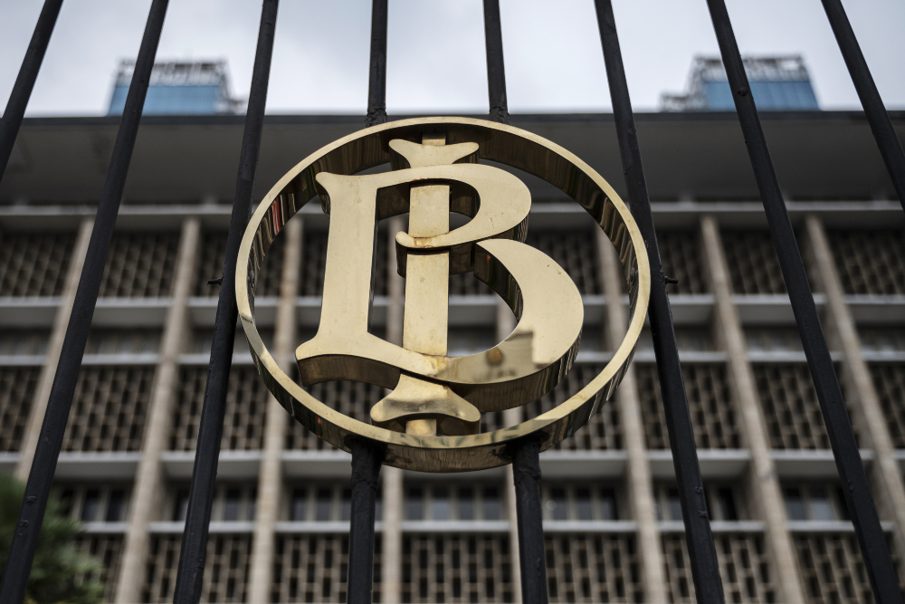Gold circular monogram (LB) centered on a black gate with a modern building in the background.
