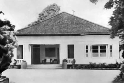 Single-story house with a wide front porch and steps, flanked by trees and a low front wall.