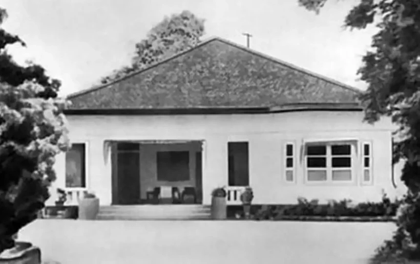 Single-story house with a wide front porch and steps, flanked by trees and a low front wall.
