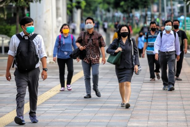People walking on a city sidewalk while wearing face masks; diverse group in business and casual attire carry bags and backpacks.