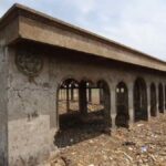 Abandoned concrete building with arched openings in a desolate, rubble-strewn landscape.