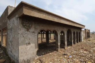 Abandoned concrete building with arched openings in a desolate, rubble-strewn landscape.