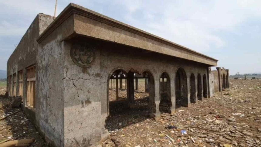 Abandoned concrete building with arched openings in a desolate, rubble-strewn landscape.