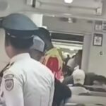 Uniformed officer standing in the aisle of a crowded airplane cabin, with passengers seated around and crew in the background.