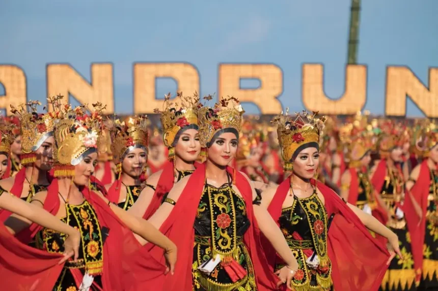 Group of women in ornate traditional costumes dancing in a festival parade, wearing gold headdresses and red capes against a blue sky background.