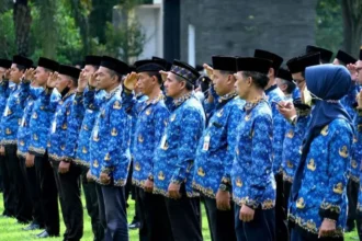 Group of people in blue batik uniforms standing in a line outdoors, many saluting during a formal ceremony.