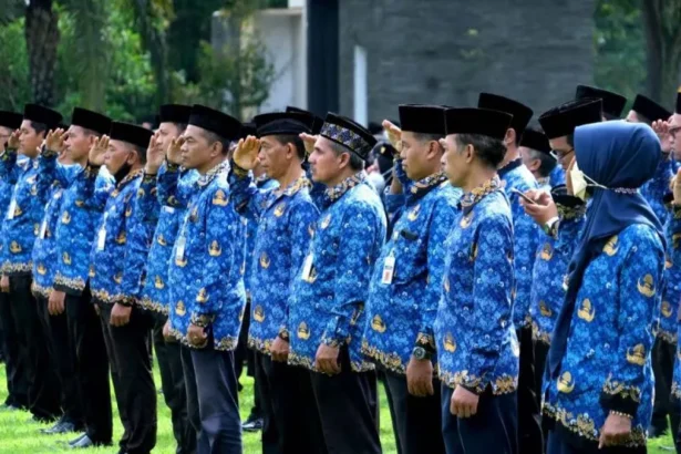 Group of people in blue batik uniforms standing in a line outdoors, many saluting during a formal ceremony.