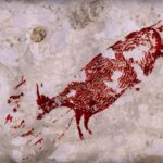 Red stencil of a dead animal spray-painted on a pale stone wall (graffiti)