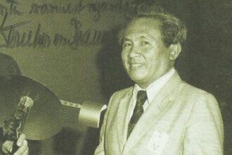 Smiling man in a light suit and tie stands at a podium during a formal event at a conference or ceremony.