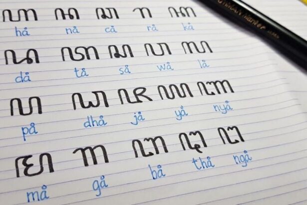 Notebook page with large black stylized characters arranged in rows, blue phonetic readings beneath each, and a black pencil resting on the top right.