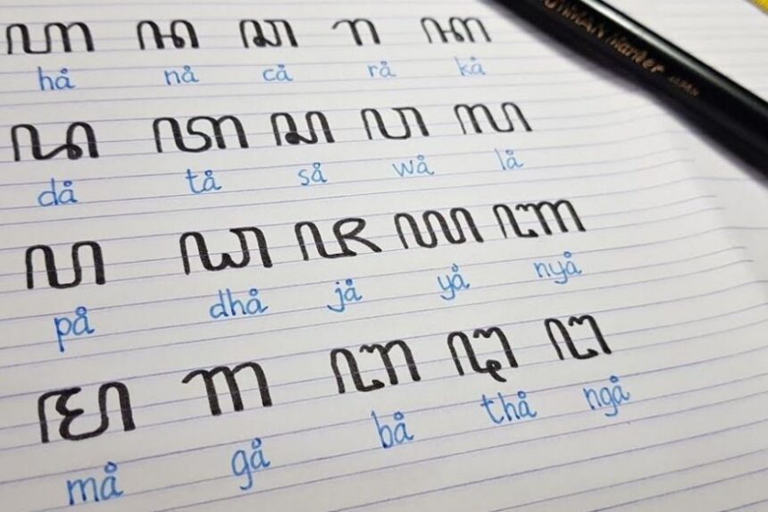 Notebook page with large black stylized characters arranged in rows, blue phonetic readings beneath each, and a black pencil resting on the top right.