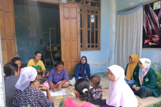 Group of women and children sit in a circle on a mat outside a blue house, likely a community gathering or lesson.