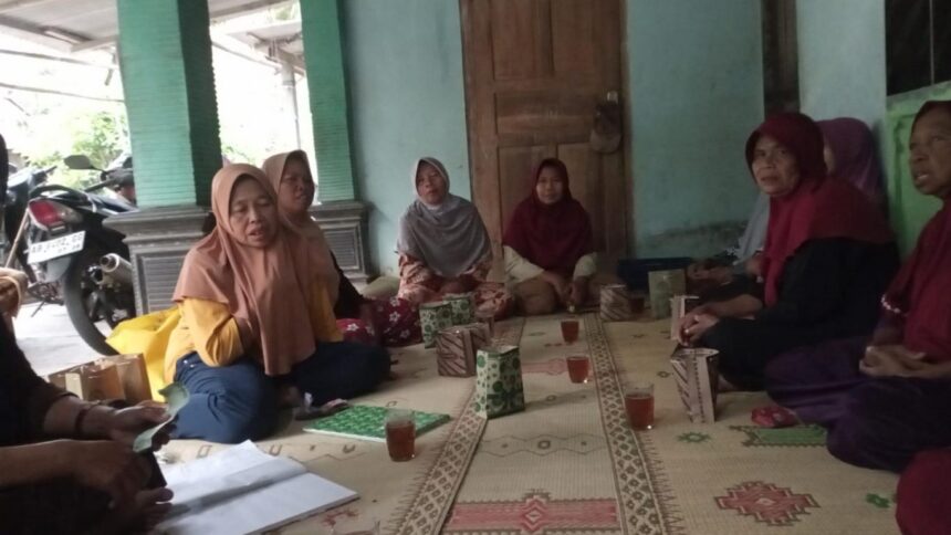 Group of women wearing hijabs sit cross-legged on a patterned mat in a circle, sharing tea and snacks in a doorway-adjacent room.