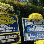 Three large flower-decorated condolence boards with blue and yellow motifs displayed outdoors.