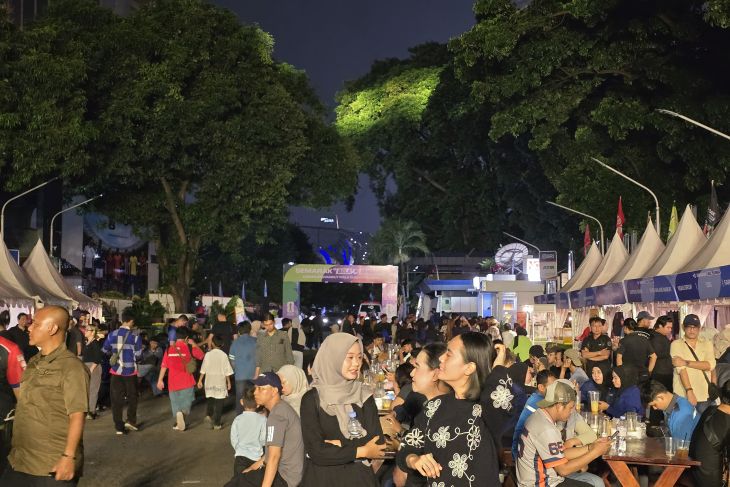 semarak bola gembira by ANTARANEWS 2 - Mabur.co Night market scene at night with tents, string lights, and a crowd gathered around food stalls and tables along a tree-lined street.