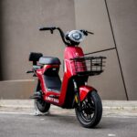 Red scooter with a front basket parked on a street in front of a brown wall, showing the 'UNITED' branding on the body.