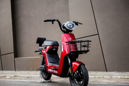 Red scooter with a front basket parked on a street in front of a brown wall, showing the 'UNITED' branding on the body.