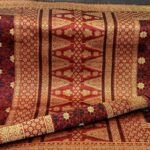 Decorative red and gold patterned rug with intricate floral motifs, partially rolled up