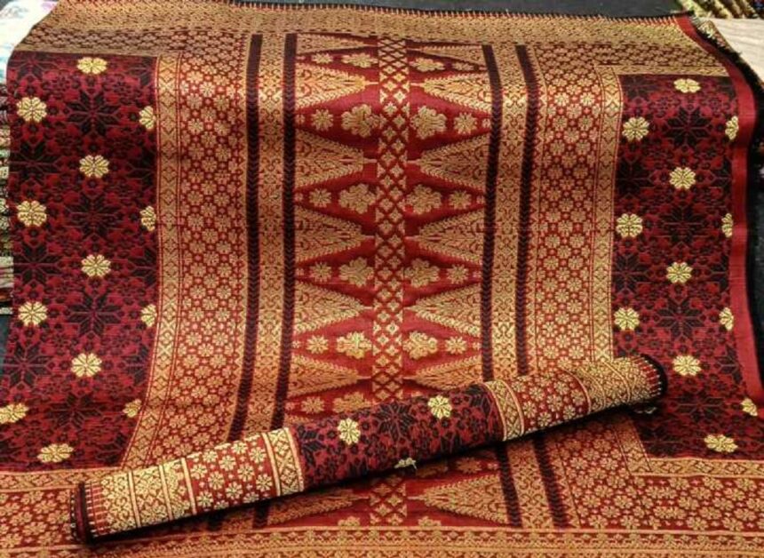 Decorative red and gold patterned rug with intricate floral motifs, partially rolled up