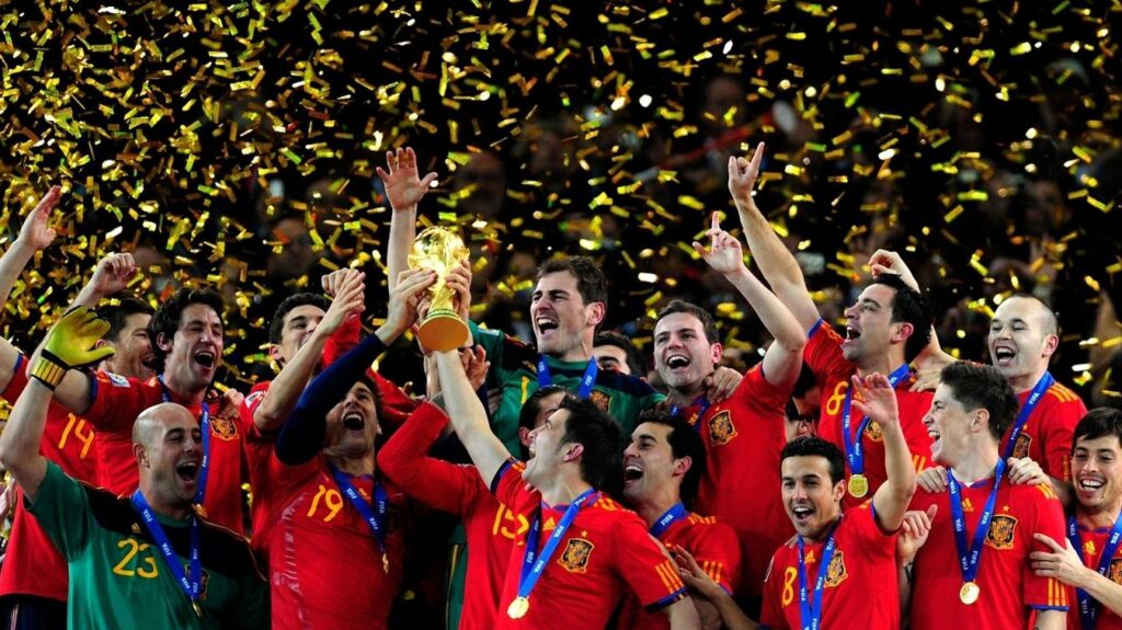 spain lift 2010 trophy by UEFA - Mabur.co Spain national team celebrates winning a trophy with gold confetti falling around them and medals around their necks.