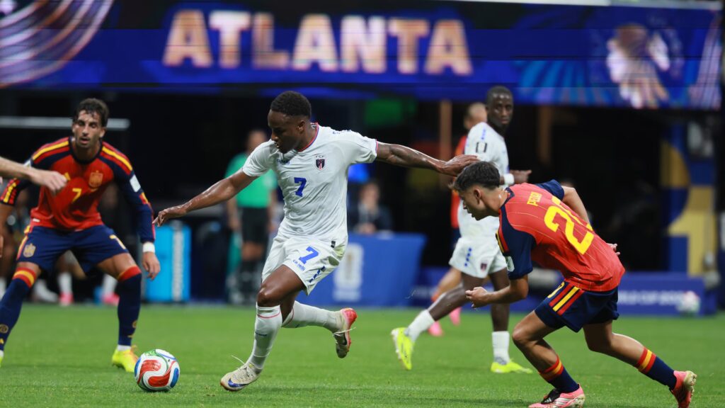 spain vs cae verde by ajc com - Mabur.co Soccer match scene with a player in a white kit (#7) reaching for the ball as opponents in red attack on a green pitch.