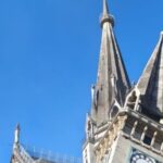 Stone Gothic church with tall pointed spires against a clear blue sky, showcasing ornate architectural details and buttresses.