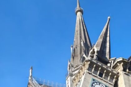 Stone Gothic church with tall pointed spires against a clear blue sky, showcasing ornate architectural details and buttresses.