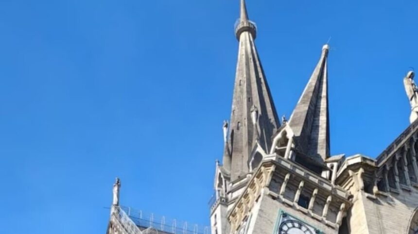 Stone Gothic church with tall pointed spires against a clear blue sky, showcasing ornate architectural details and buttresses.