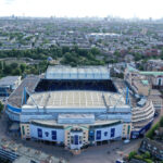 Aerial view of a large blue-and-white stadium surrounded by trees, streets, and dense city housing.