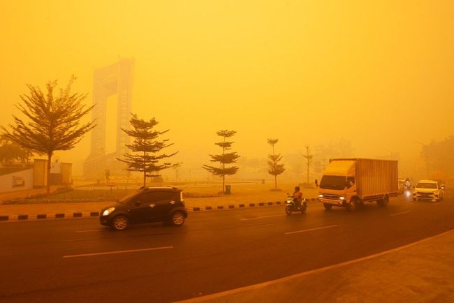 City street shrouded in thick orange smog with cars, motorcycles, and a truck visible on the road.