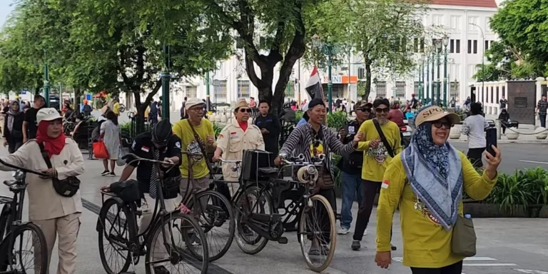 Group of people with bicycles gathered in a city square, some wearing yellow shirts and hats, taking photos and chatting.