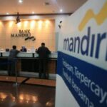Bank Mandiri counter area with customers at the service desk and a large Mandiri banner in the foreground.