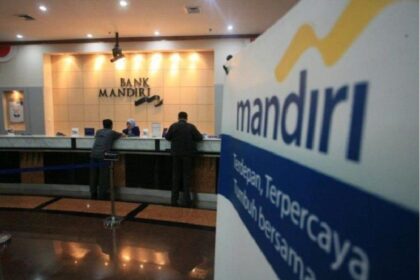 Bank Mandiri counter area with customers at the service desk and a large Mandiri banner in the foreground.