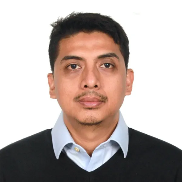 szxA - Mabur.co Professional head-and-shoulders portrait of a man in a light blue button‑down shirt and dark sweater against a white background.