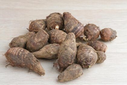 Pile of dirty taro roots on a light wooden surface