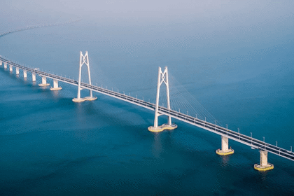 Suspension bridge spanning a calm blue ocean, featuring tall white towers and curved approach leads over the water.