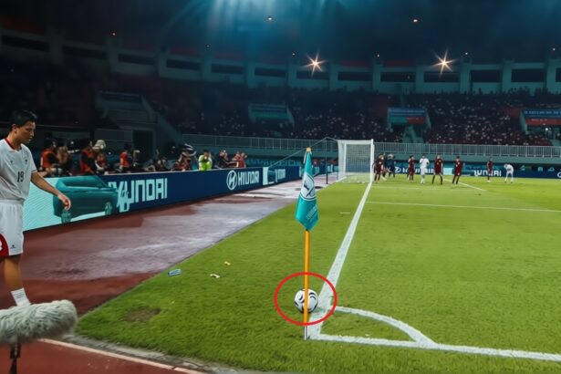 Soccer corner; a ball rests near the flag at the corner of the field with players and spectators in the background.