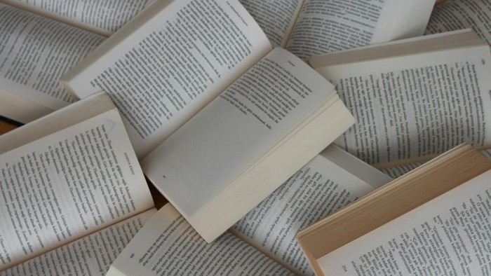 Several paperback books opened to pages, scattered in a pile and full of text.